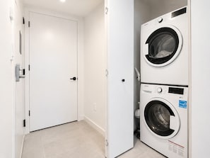 Une buanderie avec deux machines à laver superposées, une porte blanche et un sol carrelé.