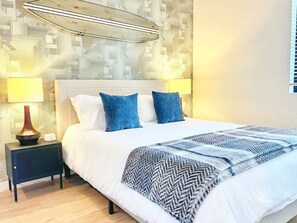 Een net opgemaakt bed met een geborreld deken, een bedlampje en een muur met een geometrisch patroon.