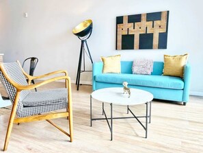 Een woonkamer met een blauwe bank, een ronde salontafel en een houten stoel.