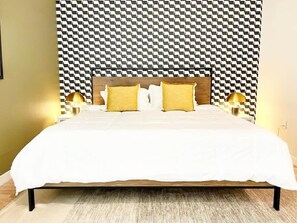 Ein Bett mit weißer Bettdecke, zwei gelben Kissen und einem Holz-Kopfbrett an einer Wand mit Muster.