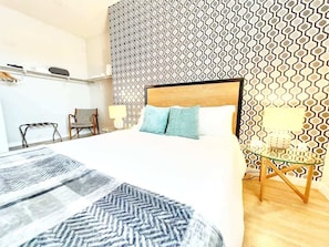 Ein modernes Hotelzimmer mit einem großen Bett, einem Holzkopfstück, einer Wand mit Muster und einem Glastisch sowie einem Stuhl.