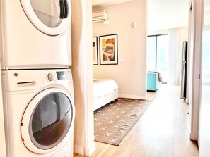 Ein Waschbereich mit Waschmaschine, ein Bett mit gemustertem Teppich und eine Küchenzeile mit Kühlschrank.