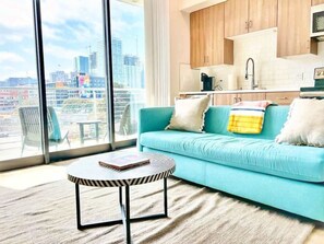 Ein modernes Wohnzimmer mit einer Couch, einem Couchtisch und Blick auf eine Stadtlandschaft durch große Fenster.