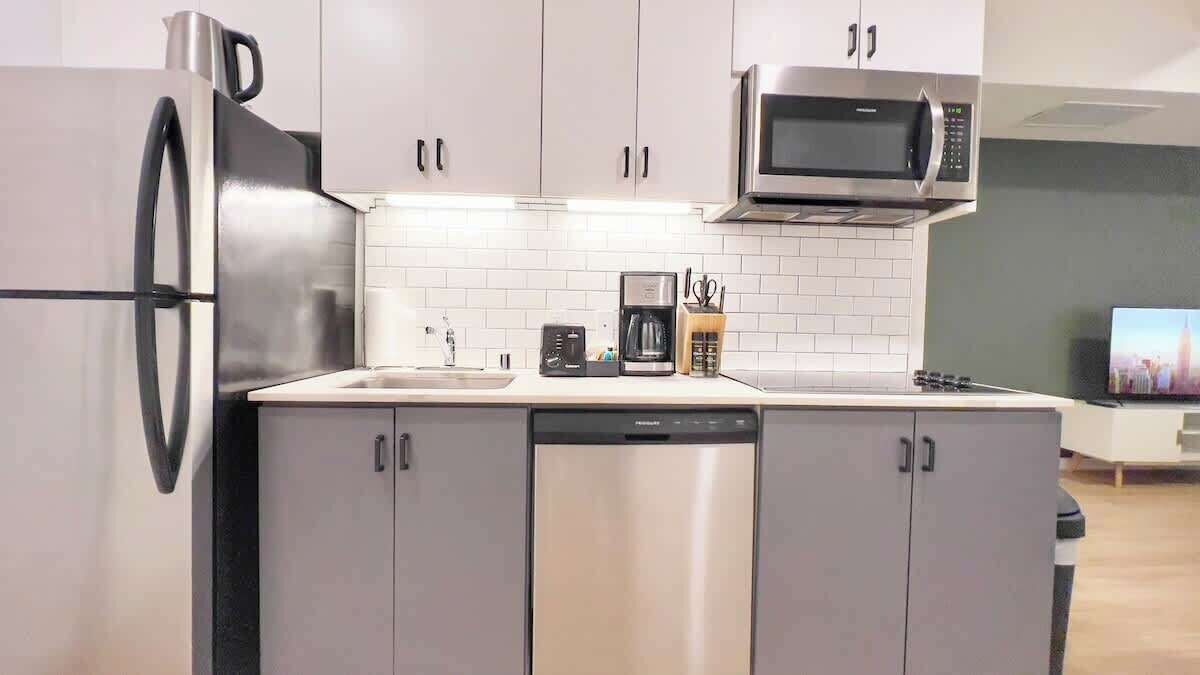 A modern kitchen with stainless steel appliances, white cabinetry, and a tiled backsplash.