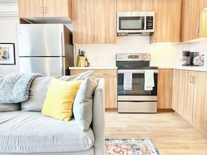 Eine moderne Küche mit Edelstahlgeräten, Holzschränken und einem grauen Sofa mit gelben Kissen.