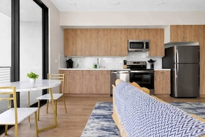 A modern kitchen with wooden cabinets, stainless steel appliances, and a dining area with a round table and chairs. - Modern Downtown Retreat | Balcony + Rooftop Views (San Diego)
