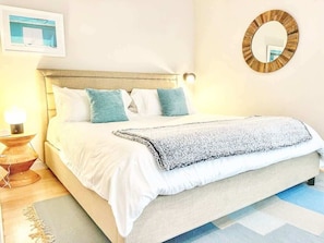 Ein Schlafzimmer mit Bett, Kissen, Nachttisch, Lampe, Spiegel und Teppich.
