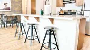 A modern kitchen with a central island, bar stools, and a microwave.