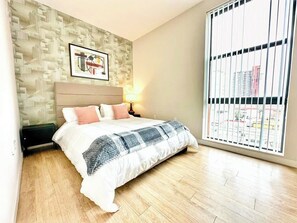 Ein Schlafzimmer mit Bett, Kopfstütze, Wandbild, Fenster mit Jalousien und Holzboden.