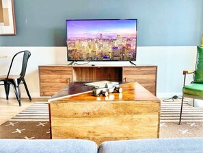 Ein modernes Wohnzimmer mit Flachbildfernseher, Couchtisch aus Holz und Blick auf die Stadt.