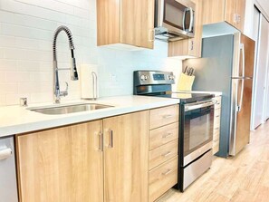 Eine Küche mit Holzausstattung, einem Edelstahlkühlschrank, einer Mikrowelle und einem Backofen.