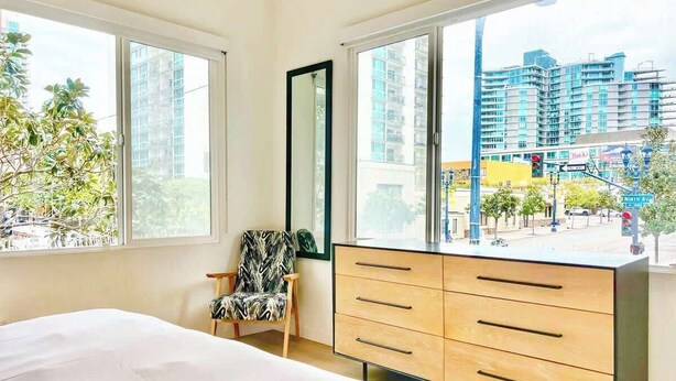 Ein Schlafzimmer mit einem großen Bett, einem Schminktisch, einem Sessel und einem Fenster mit Blick auf die Stadt.