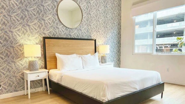 Un dormitorio con cama, mesitas de noche, espejo y ventana con vistas.