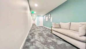 Un pasillo con un sofá color beige, alfombra estampada, paredes color aguamarina y cuadros en la pared.
