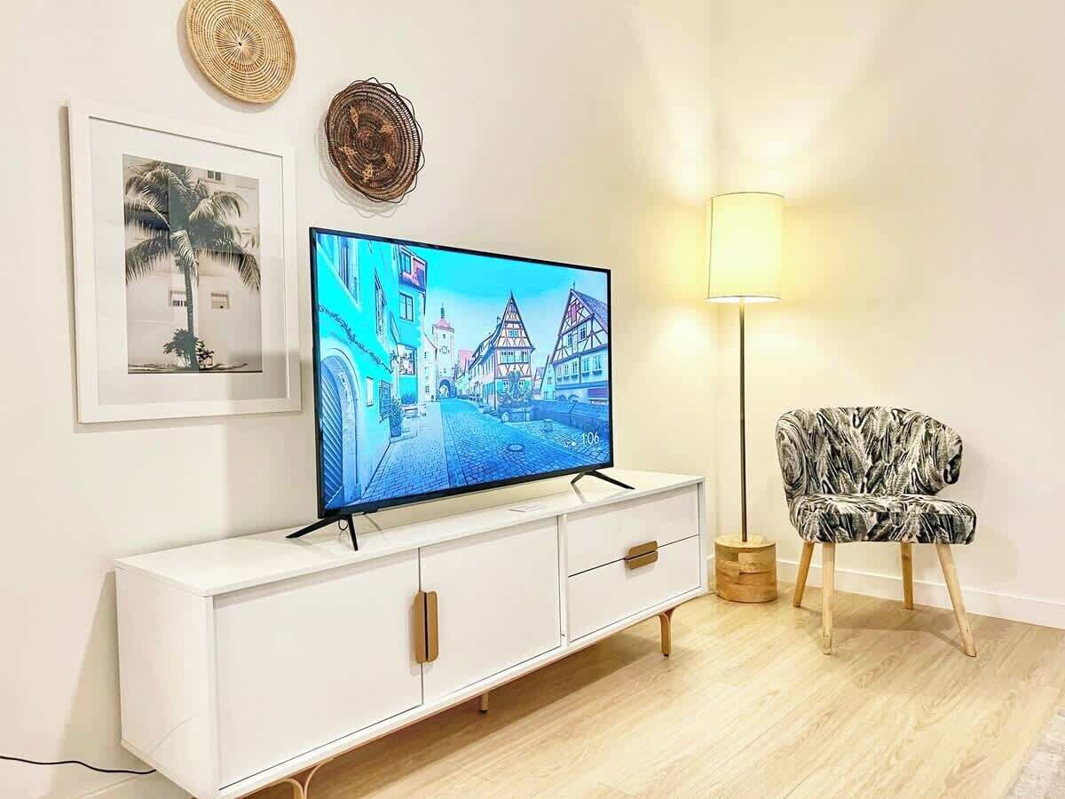 Uma sala de estar moderna com televisão de tela plana, um armário branco, uma poltrona estampada e um abajur.