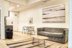 Un soggiorno moderno con un divano grigio, un tavolino rotondo, un tappeto a righe, un'area pranzo con un tavolo piccolo e sedie, e un grande quadro astratto appeso al muro.