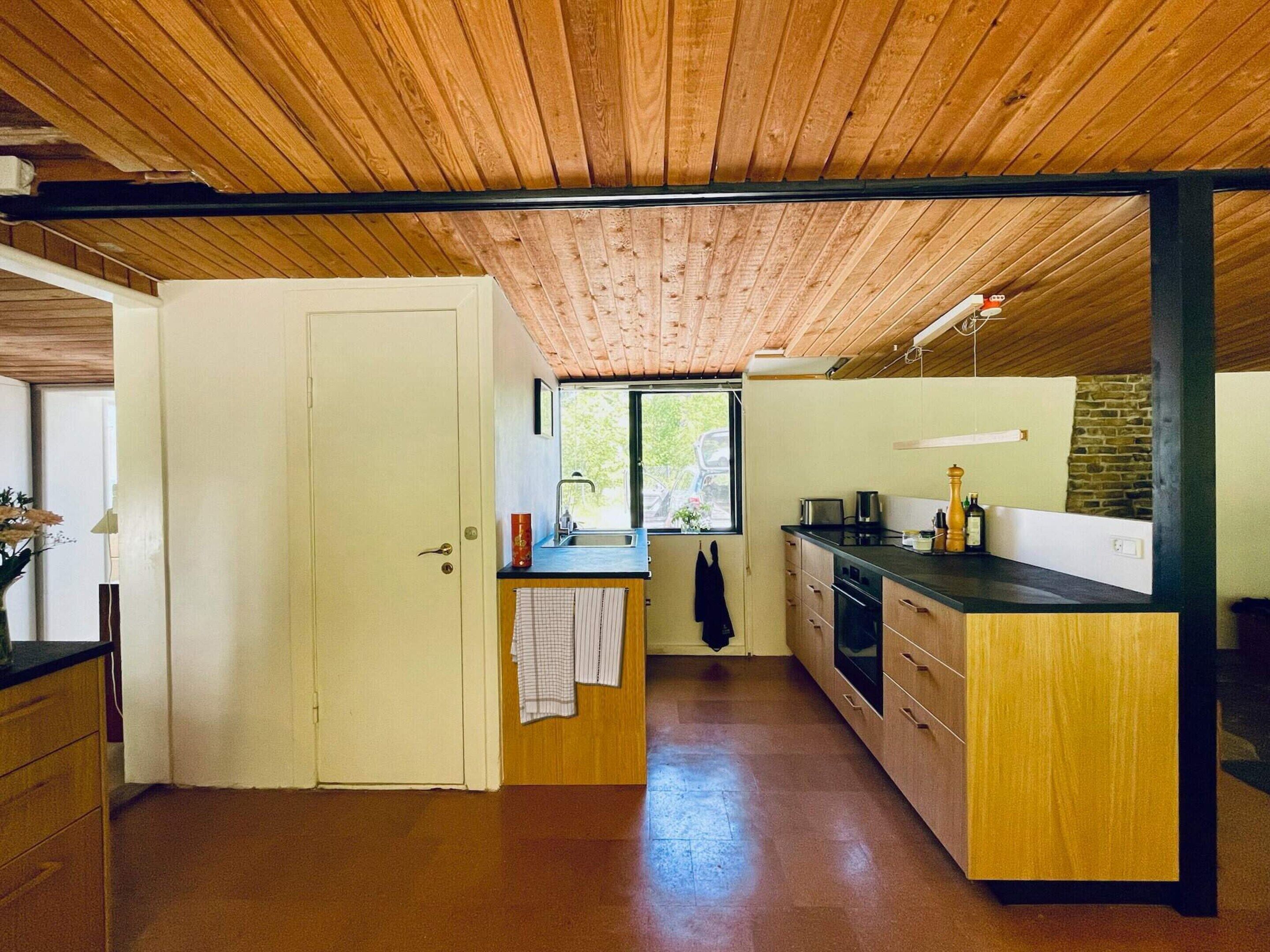A compact kitchen with wooden cabinetry, a sink, and a window overlooking a green landscape.