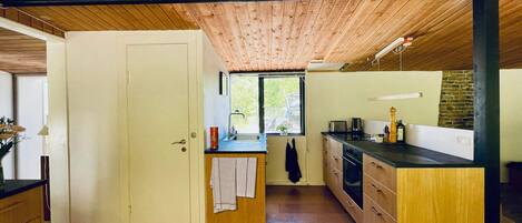 A compact kitchen with wooden cabinetry, a sink, and a window overlooking a green landscape.