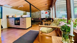 Eine moderne Küche mit Holzschränken, ein Essbereich mit einer Couch und einem Tisch, und ein großes Fenster, das natürliches Licht hereinlässt.