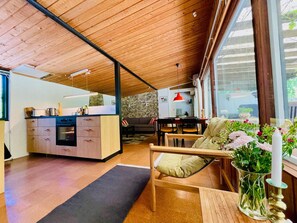 A modern kitchen with wooden cabinets, a dining area with a sofa and table, and a large window providing natural light. - 4 Star Holiday Home in Vaeggerlose (Vaeggerlose)