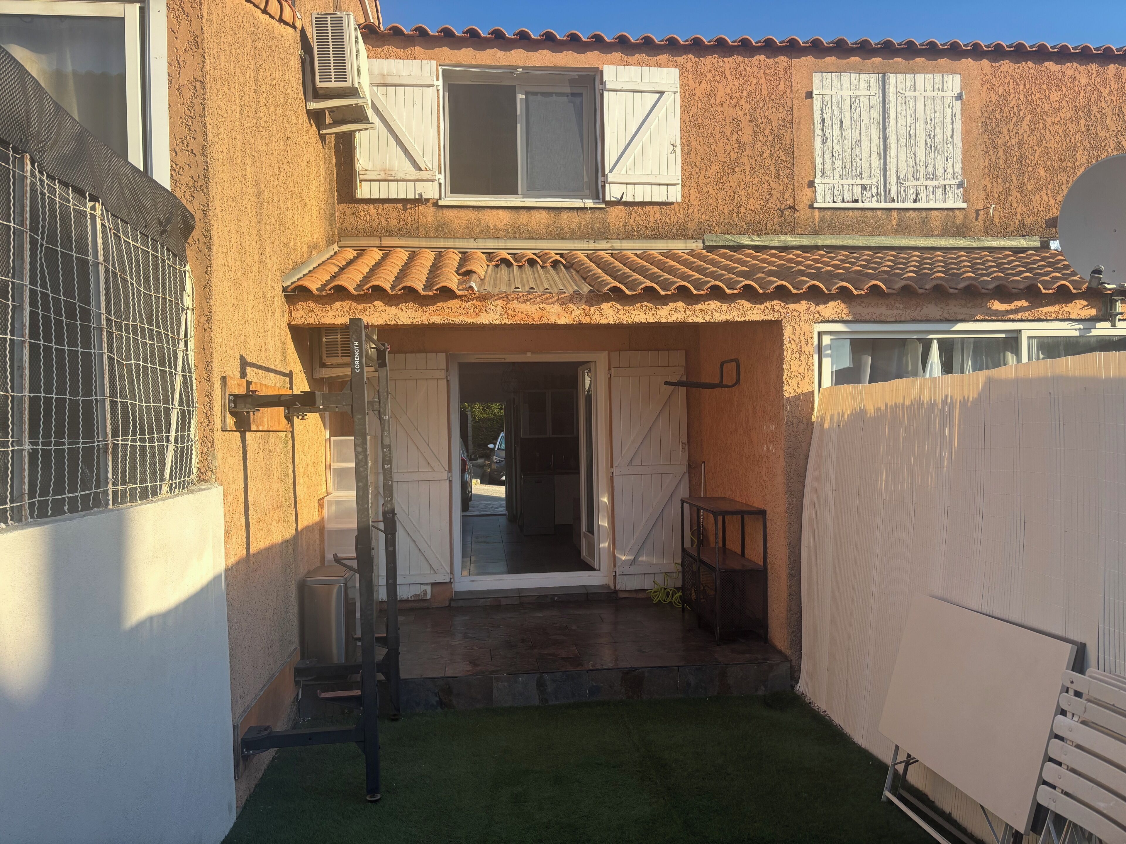 Une maison à deux étages, avec un toit en tuiles, une terrasse couverte et une cour clôturée.