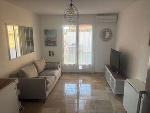 Ein Wohnzimmer mit einer Couch, einem Fernseher, einer Deckenleuchte, einer Tür mit Blick und einer Klimaanlage.