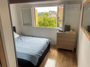 Ein Schlafzimmer mit einem Bett, einer Kommode, einem Fenster mit Blick auf Grünflächen und einer Klimaanlage.
