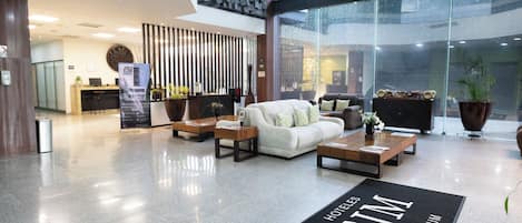 Un vestíbulo de hotel con mostrador de recepción, zona de estar y un amplio ventanal.