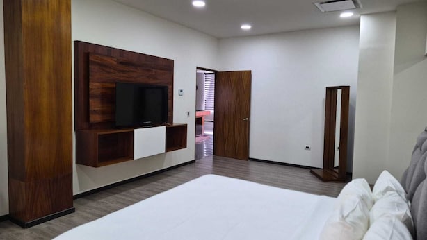 A modern bedroom with a large bed, a TV mounted on a wooden panel, and a wardrobe.