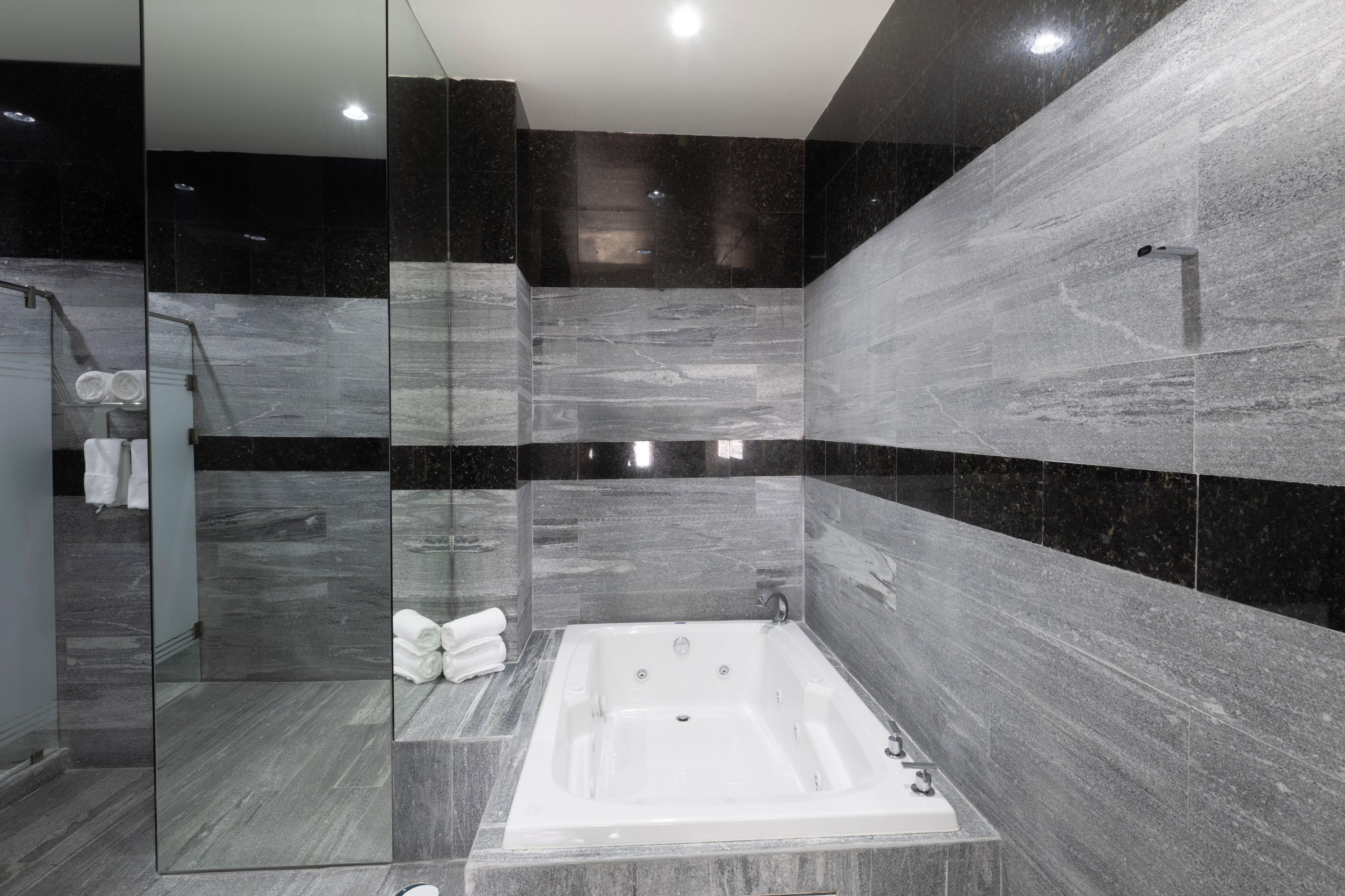 Un baño moderno con una bañera independiente, cabina de ducha con mampara de vidrio y paredes de mármol.