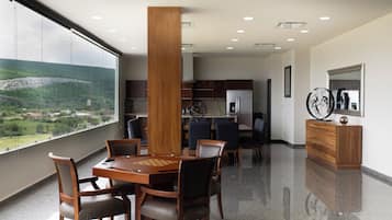 Un comedor moderno con mesa y sillas de madera, una cocina al fondo y vistas a un paisaje montañoso a través de amplias ventanas.