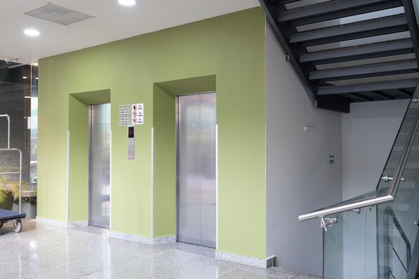An interior with a green wall, two elevators, a digital display, and a staircase.