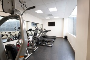 A gym with exercise equipment, a large mirror, and a TV on the wall.