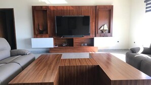 A modern living room with a flat-screen TV, wooden entertainment unit, and two grey sofas.