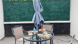 A round glass table with chairs, a table umbrella, and a meal with plates, cups, and a bottle.