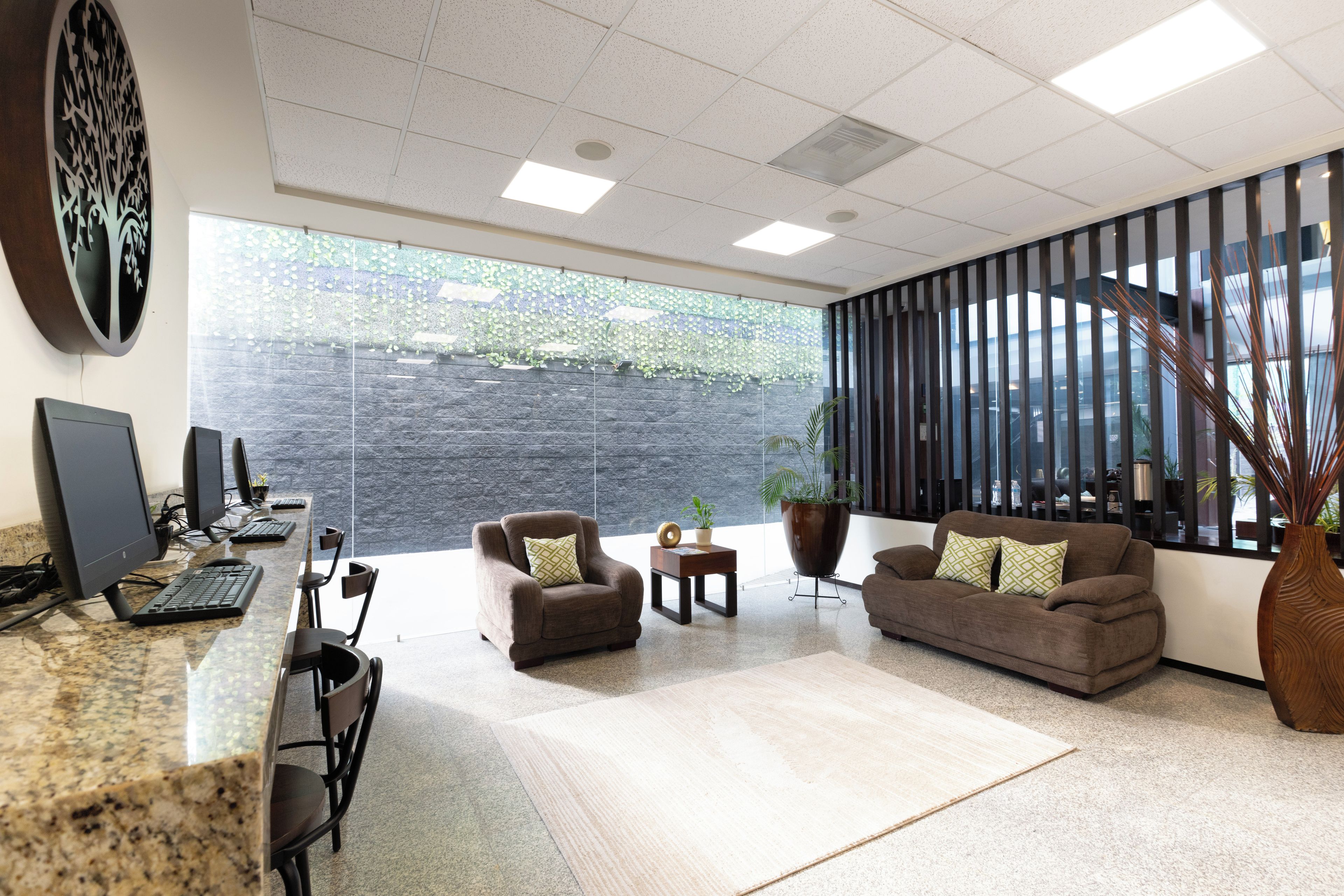 Un espacio de oficina moderno con un mostrador de recepción, dos sillones, un sofá y un ventanal con vistas a zonas verdes.