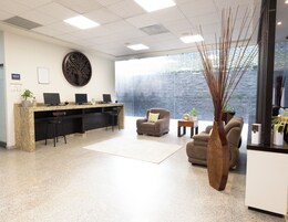 Zona de recepción con mostrador, dos monitores de computadora, una silla, un sofá y un amplio ventanal con vistas.