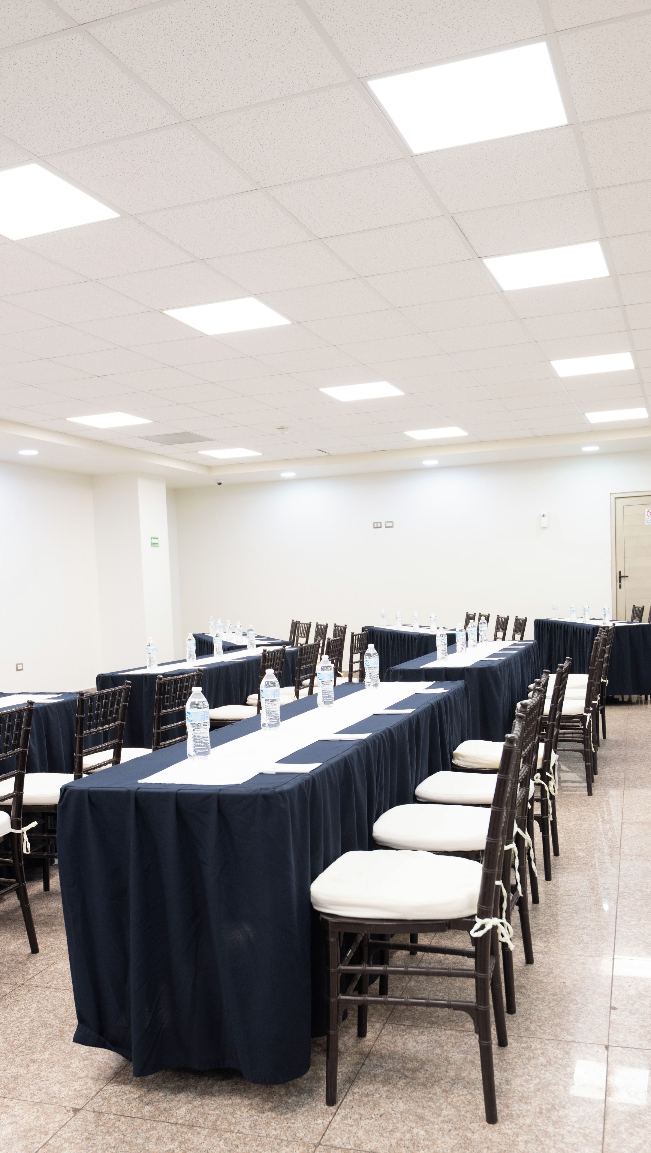 Un salón de conferencias con varias mesas y sillas, equipado con botellas de agua.