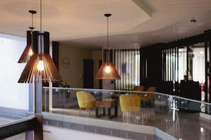 Un intérieur moderne avec des luminaires suspendus, une rambarde en verre et des chaises jaunes dans un espace détente.