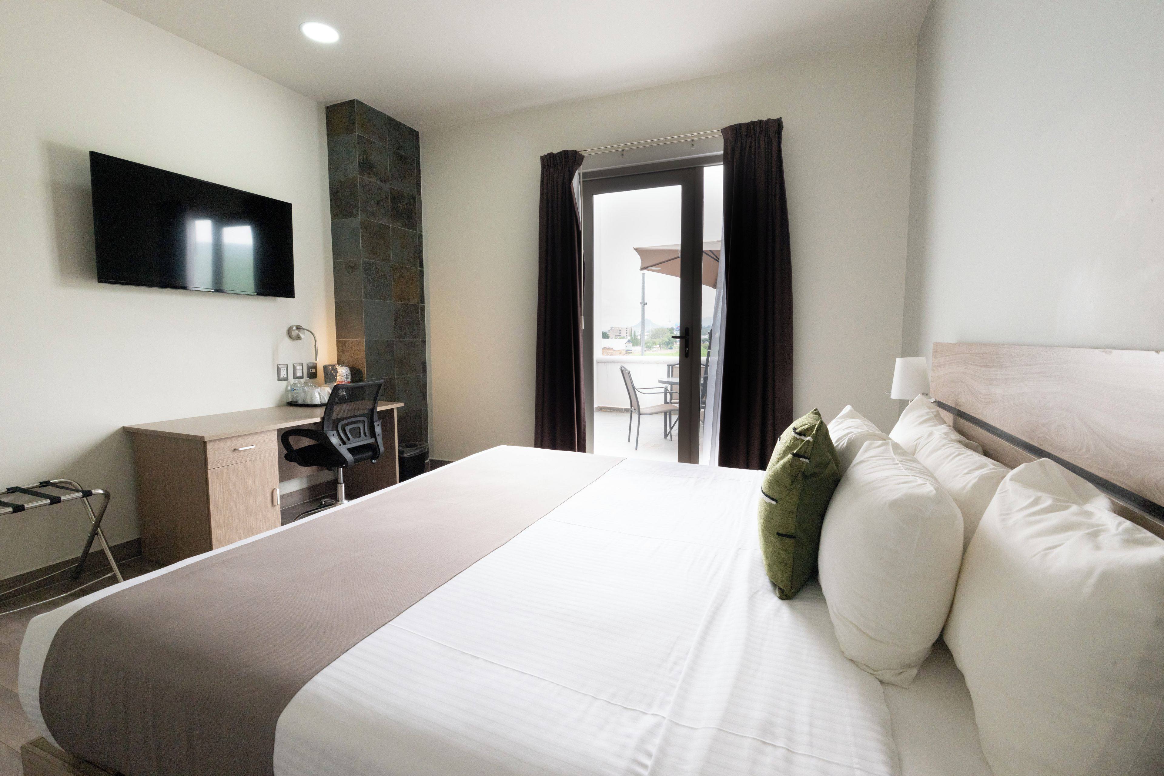 Habitación de hotel con cama, escritorio, televisión y vistas al exterior.