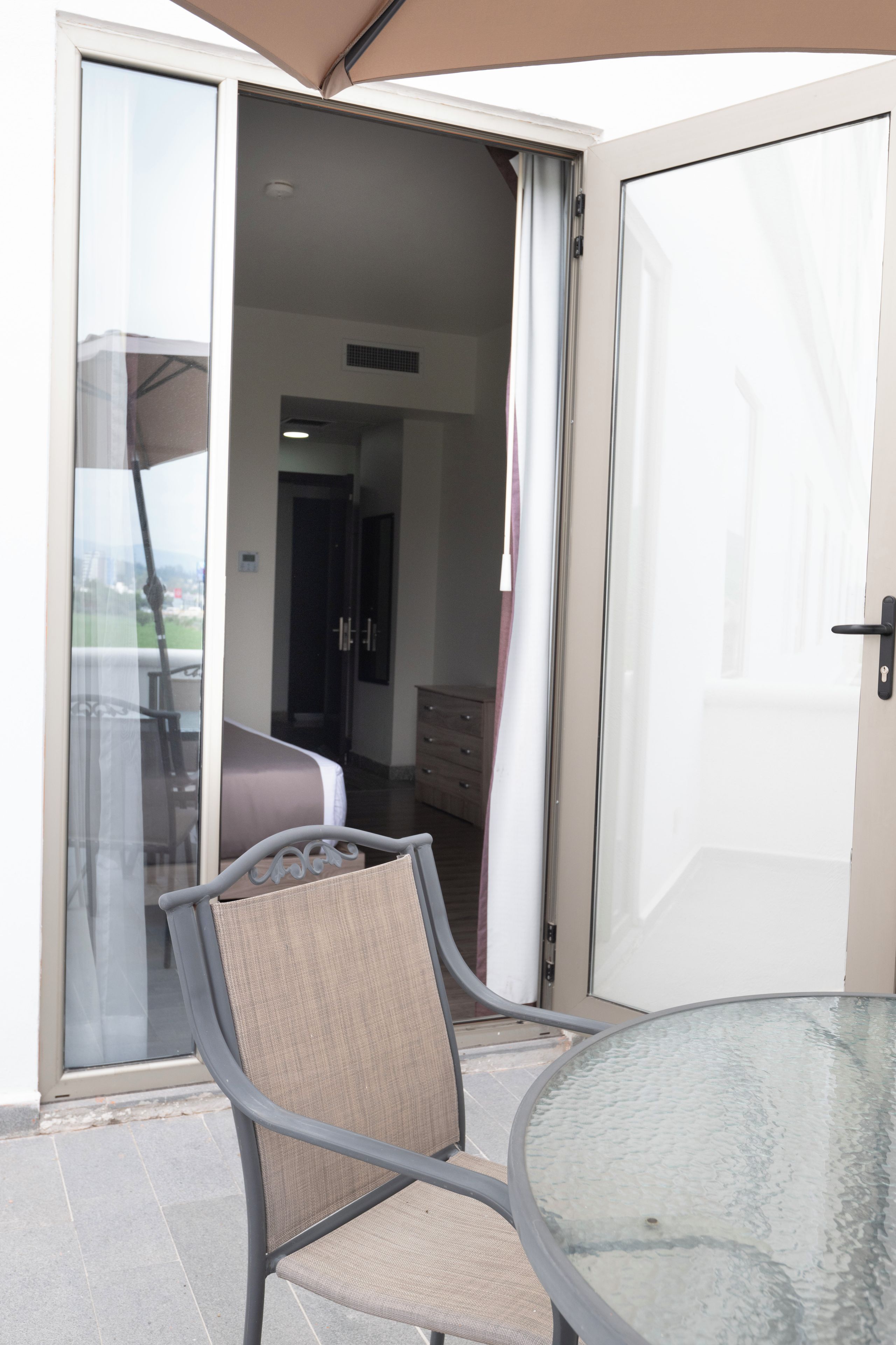 Une chambre dotée d’une porte-fenêtre coulissante donnant sur un balcon, d’un lit, d’une commode et d’une chaise.
