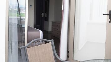 Une chambre dotée d’une porte-fenêtre coulissante donnant sur un balcon, d’un lit, d’une commode et d’une chaise.