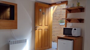 A compact room with a wooden door, a small refrigerator, a microwave, and a built-in shelf with dishes. - Morada Bem Me Quer (Canela)