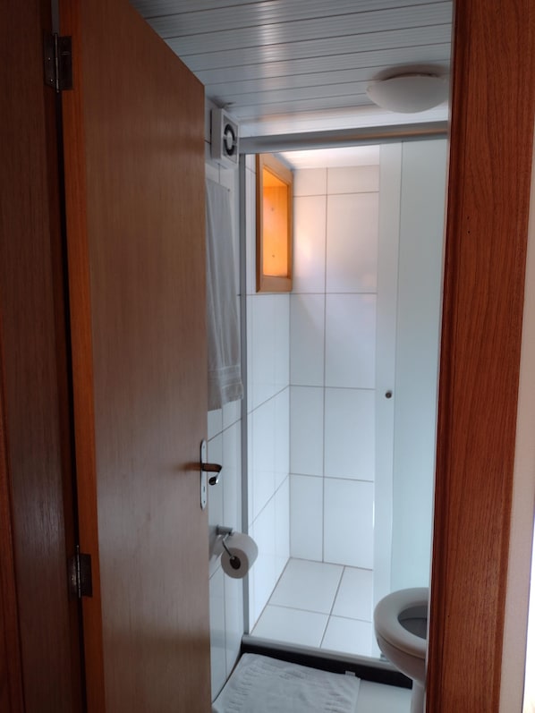 A small, compact bathroom with white tiles, a toilet, and a shower area.