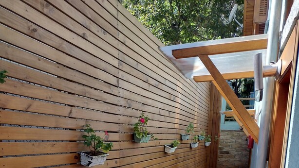 A wooden wall with potted plants, a brick pathway, and a wooden structure with a glass roof. - Morada Bem Me Quer (Canela)
