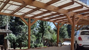 A covered parking area with a brick floor, wooden beams, and a white car parked. - Morada Bem Me Quer (Canela)