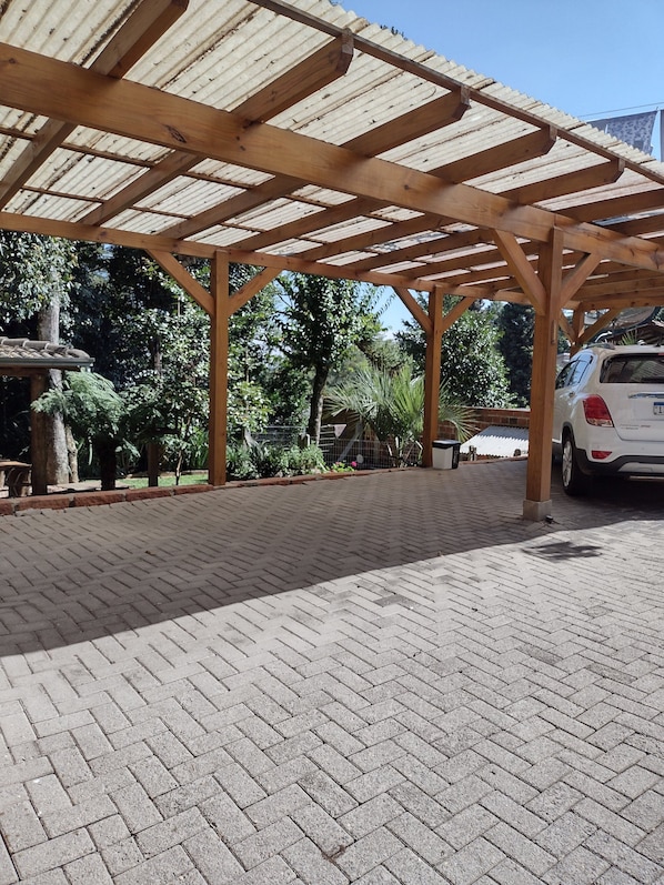 A covered parking area with a brick floor, wooden beams, and a white car parked.
