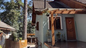A house with a tiled roof, a wooden porch, and a large tree in the background. - Morada Bem Me Quer (Canela)