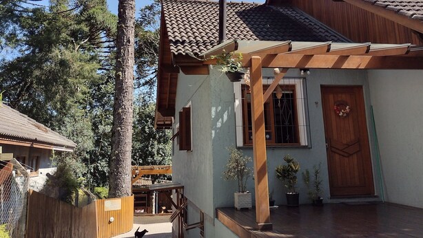 A house with a tiled roof, a wooden porch, and a large tree in the background. - Morada Bem Me Quer (Canela)