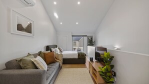 A modern, compact bedroom with a bed, bedside table, and a large window.